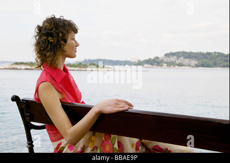 Eine Frau sitzt auf einer Bank mit Blick auf das Meer Stockfoto