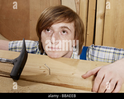 Ein junger Mann hinter einem verbogenen Nagel in Holz Stockfoto