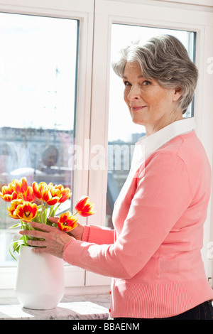 Eine ältere Frau Anordnen von Blumen in einer vase Stockfoto