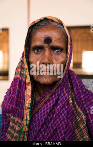 Eine alte Frau mit grauem Star sitzt und wartet auf ihren Zug auf der Plattform von Badami Bahnhof in Indien. Stockfoto