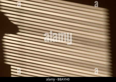 Schatten, die aus einem Fenster und starkem Sonnenlicht fällt auf eine Wand durch eine Jalousie Stockfoto