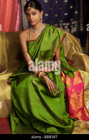 Frau trägt Sari, umgeben von Sari-Stoff, verziert mit Henna-Tattoos, Schmuck und bindi Stockfoto