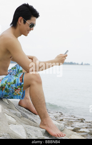 Mann sitzt am Strand, Blick auf Handy Stockfoto