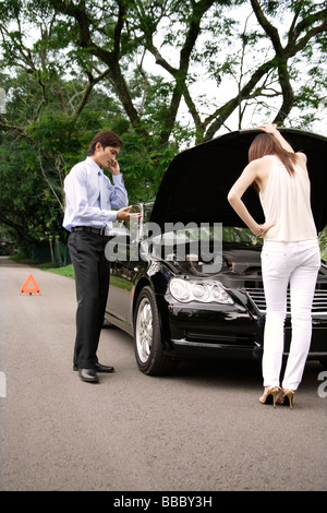 Frau, die unter die Haube des Autos beim Mann Gespräche am Telefon Stockfoto