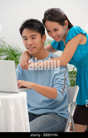 Junge Frau stützte sich auf die Schulter des Mannes am computer Stockfoto