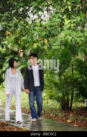 Ein junges Paar an den Händen halten und schlendern Sie durch einen Gartenweg zusammen Stockfoto