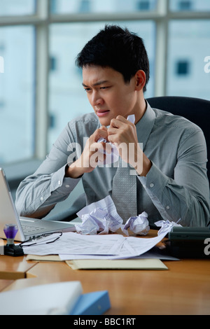 Ein Mann sieht gestresst, als er an seinem Schreibtisch arbeitet Stockfoto