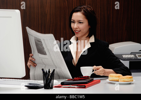 Eine Frau nimmt sich eine Auszeit am Arbeitsplatz und liest die Zeitung Stockfoto