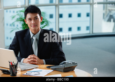Ein Mann schaut in die Kamera, als er an seinem Schreibtisch sitzt Stockfoto