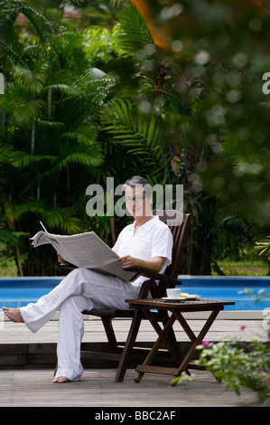 Reifer Mann sitzt neben Schwimmbad, Zeitung lesen Stockfoto