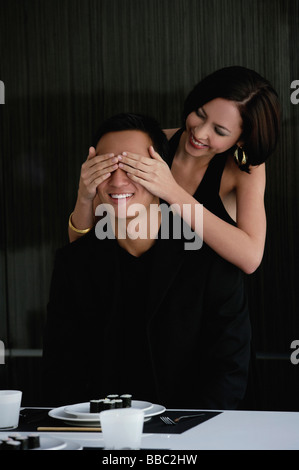 Eine Frau bedeckt ihre Freunde Augen, wie sie bereitet ihn mit Abendessen überraschen Stockfoto