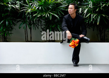 Ein Mann sitzt und wartet, während er einen Blumenstrauß hält Stockfoto