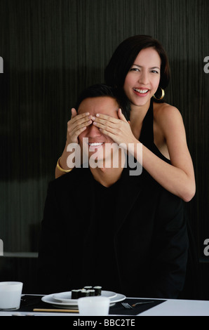 Eine Frau bedeckt ihre Freunde Augen, wie sie bereitet ihn mit Abendessen überraschen Stockfoto