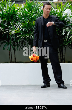 Ein Mann blickt seine Uhr, während er einen Blumenstrauß hält Stockfoto