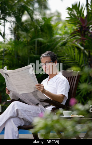 Reifer Mann sitzen im Garten, lesen Zeitung Stockfoto