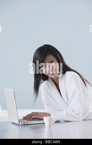 Frau mit Bademantel, lächelnd und arbeiten auf Laptop-Computer, lächelnd in die Kamera Stockfoto