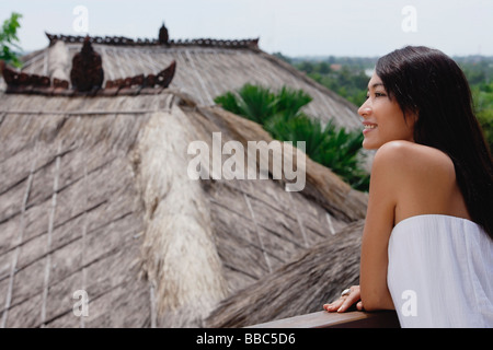 Junge Frau lehnt sich am Geländer mit Blick auf thatched Dächer Stockfoto
