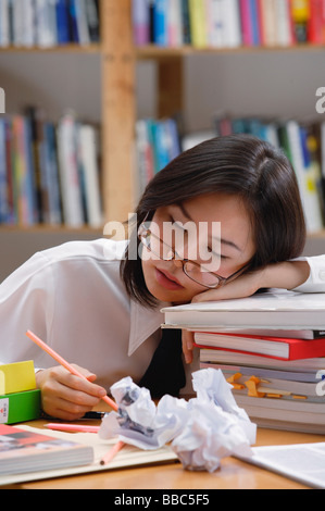 Junge Frau in Bibliothek, schlafen auf Stapel Bücher Stockfoto
