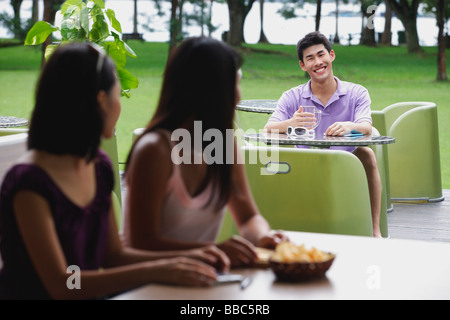 Junger Mann sitzt am Straßencafé, lächelte Frauen im Vordergrund Stockfoto