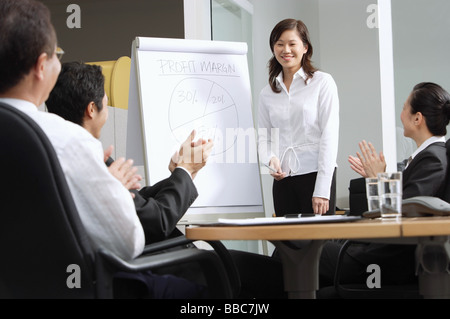 Geschäftsfrau, die neben Flipchart, Kollegen sitzen und klatschten stehend Stockfoto