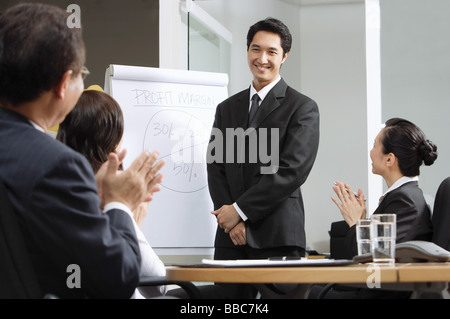 Geschäftsmann, stehen neben Flipchart, andere Führungskräfte Händeklatschen Stockfoto