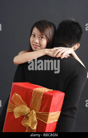 Mann hält Geschenk hinter seinem Rücken, Frau umarmte ihn über die Schulter in die Kamera schaut Stockfoto
