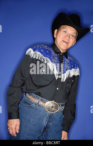 Ältere Mann gekleidet in Cowboy-Kleidung, stehend vor blauem Hintergrund Stockfoto