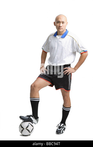 Junger Mann tragen Fußball Uniform, steht mit einem Bein auf ball Stockfoto