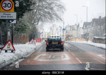 Treiber-Blick durch ein Auto Windschutzscheibe Verkehr Warteschlangen an Baustellen auf einer verschneiten Straße in England im winter Stockfoto