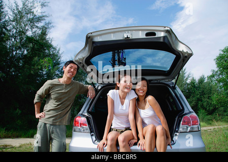 Frauen sitzen im Kofferraum des Autos, Mann stützte sich auf Auto Stockfoto