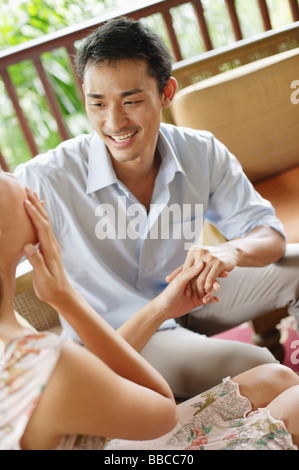 Paar sitzen Angesicht zu Angesicht, Hand in Hand, Frau mit Hand auf Gesicht Stockfoto