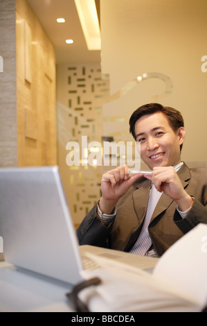 Geschäftsmann, sitzen, halten Sie Stift und lächelt in die Kamera Stockfoto