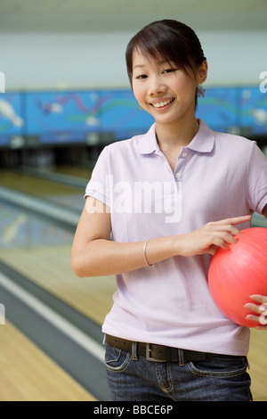 Frau auf Bowling-Bahn, Lächeln, Bowling-Kugel unter Arm halten Stockfoto
