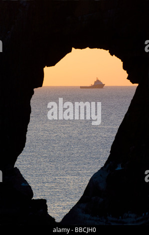 Natürlichen Felsbogen in Dunbuy Rock, Schottland, und ein Öl-Industrie Versorgungsschiff in der Ferne als Morgendämmerung bricht über der Nordsee. Stockfoto