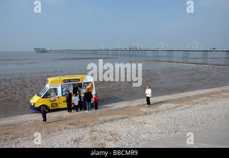 Menschen, die Warteschlangen an einem Eiswagen auf Southport Strand mit Southport Pier im Hintergrund Stockfoto