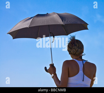 Rückansicht des jungen schwarzen Frau Beschattung selbst von der Sonne unter einem schwarzen Regenschirm Stockfoto