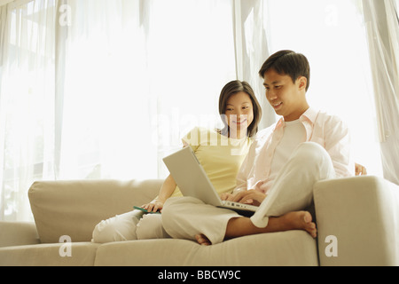Junges Paar sitzt auf dem Sofa nebeneinander mit laptop Stockfoto