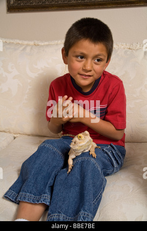 Porträt von Hispanic Junge sitzt auf der Couch mit Bearded Dragon seltsame Kreatur Kreaturen zweifelhaft, unsicher, verängstigt Herr © Myrleen Pearson Stockfoto