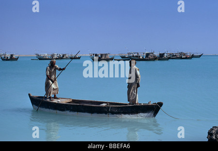 Katar Nahost Golf Staat Khor Fischer in einem hölzernen Kanu im Meer mit Fischerbooten vor Anker jenseits im Hafen Stockfoto