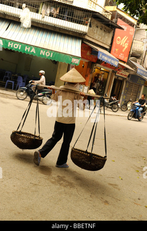 Straßenhändler mit traditionellen Conehat und Bambuskorb mit Stock in Altstadt, Hanoi, Vietnam. Stockfoto