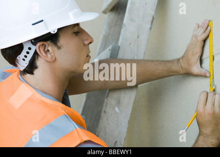 Bauarbeiter auf Leiter Kennzeichnung Messung an Wand Stockfoto