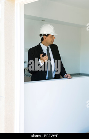 Mann im Anzug tragen Schutzhelm Walkie-talkie Fenster Ausschau halten Stockfoto