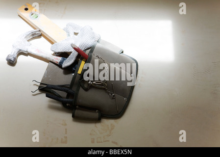 Werkzeuggürtel mit Hammer, Ebene und Handschuhe am Boden liegend Stockfoto