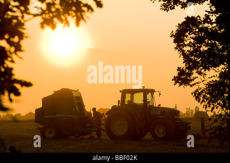 Schöne Aussicht auf ein Landwirt einen Traktor auf einem Feld bei Sonnenuntergang in der englischen Landschaft fahren Stockfoto
