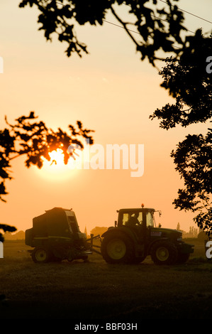 Schöne Aussicht auf ein Landwirt einen Traktor auf einem Feld bei Sonnenuntergang in der englischen Landschaft fahren Stockfoto