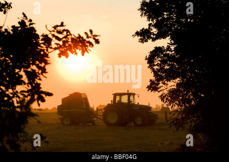 Schöne Aussicht auf ein Landwirt einen Traktor auf einem Feld bei Sonnenuntergang in der englischen Landschaft fahren Stockfoto
