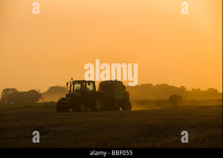 Schöne Aussicht auf ein Landwirt einen Traktor auf einem Feld bei Sonnenuntergang in der englischen Landschaft fahren Stockfoto