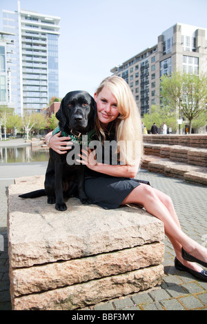 Blondine mit weißen kaukasischen Frau mit schwarzen Labrador Guide Hund in eine urbane Parklandschaft. Stockfoto