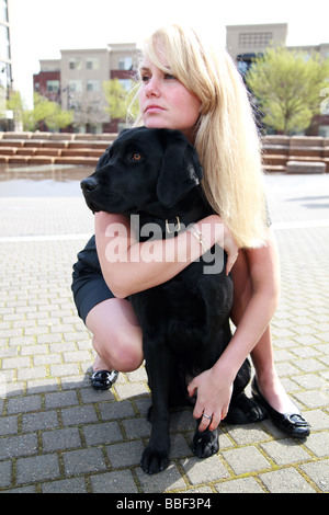 Blondine mit weißen kaukasischen Frau mit schwarzen Labrador Guide Hund in eine urbane Parklandschaft. Stockfoto