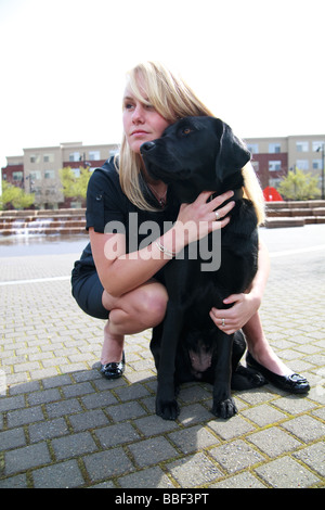 Blondine mit weißen kaukasischen Frau mit schwarzen Labrador Guide Hund in eine urbane Parklandschaft. Stockfoto